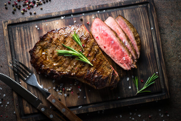 Grilled beef steak medium rare on wooden cutting board.