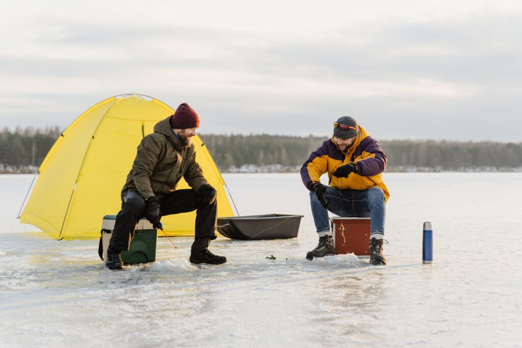 Two men sitting on their soft coolers while ice fishing